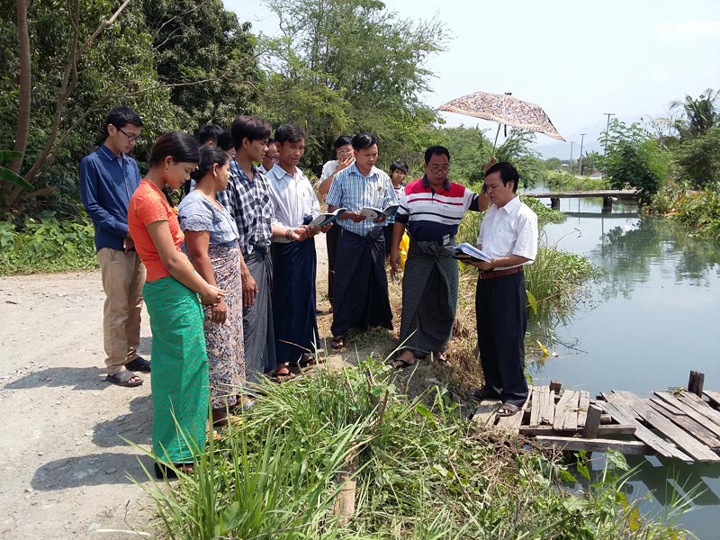 Singing hymns and sharing a message before a water baptism in Mandalay.